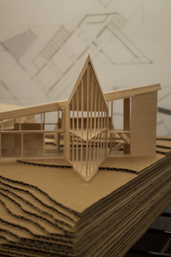 A wooden model of a building with upward sloping roofs that come to a triangular point.