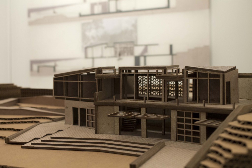 A cardboard model of a visitor's center with glass doors that swing upward to open.