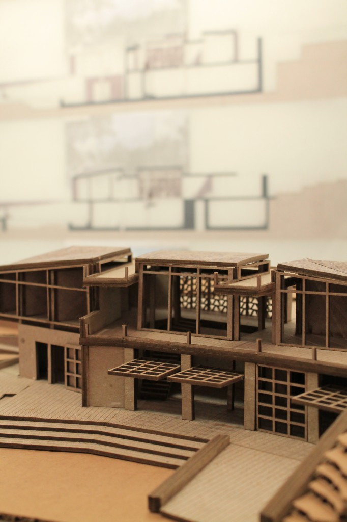 A cardboard model of a visitor's center with glass doors that swing upward to open.