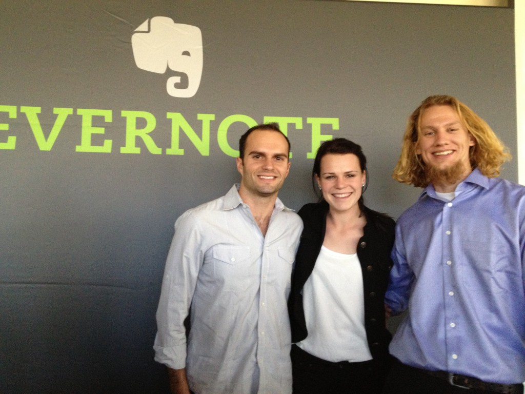 Three people stand side by side, arms around each other in front of a black background with the word "Evernote" and an elephant logo on it.